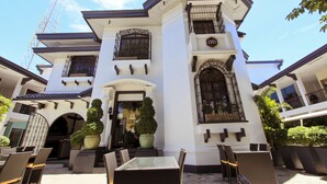 A building with a symmetrical facade, large potted plants, outdoor seating, and a visible construction crane. - The Bourke Hotel (Davao)