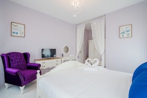 A bedroom with a bed, a purple armchair, a dresser, a television, and two wall-mounted artwork pieces. - Wan Arun Houses (Hua Hin)