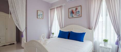 Un dormitorio con cama blanca, almohadas azules, armario blanco y dos aires acondicionados instalados en la pared.