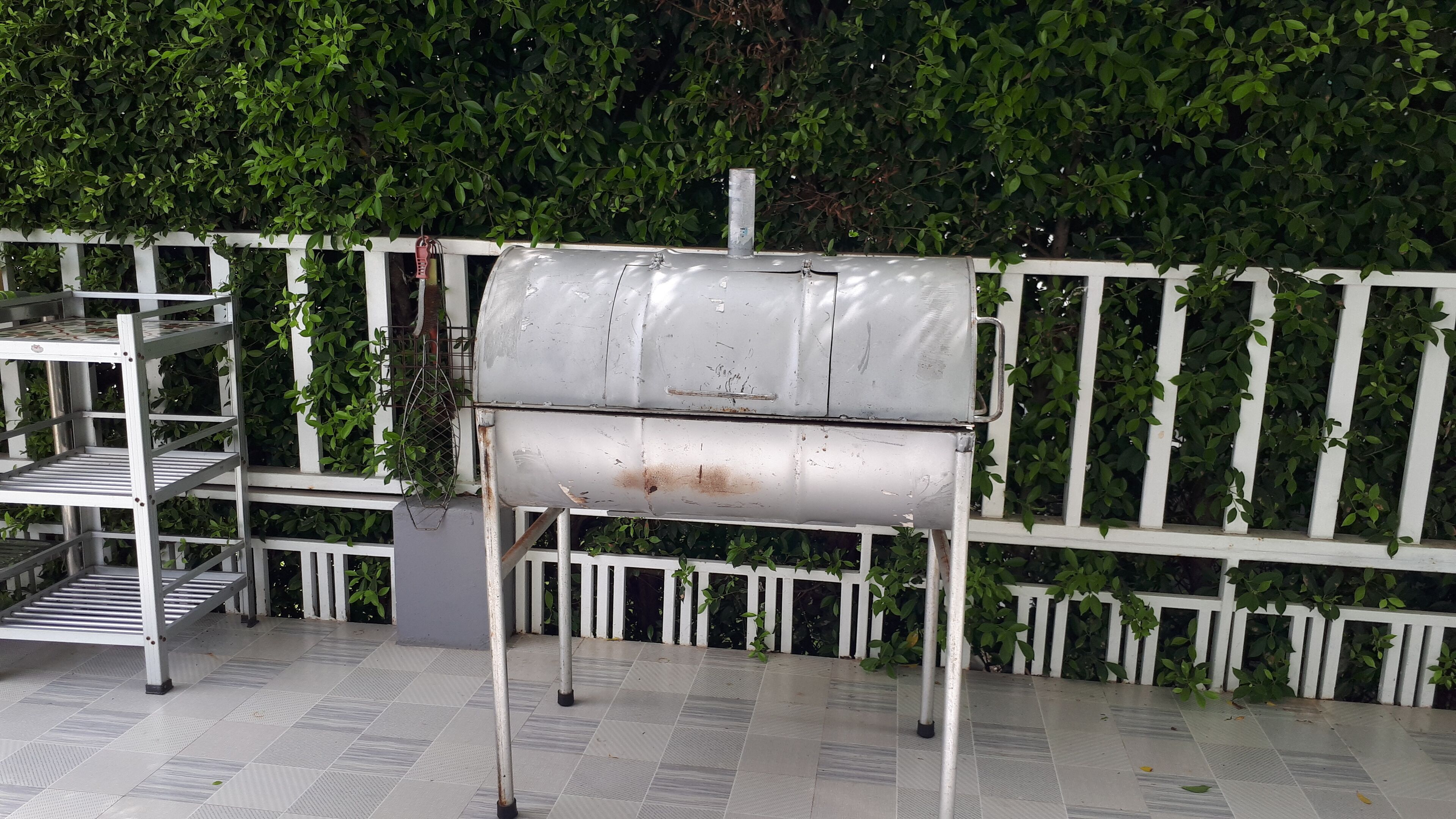 Un barbecue en métal, avec une clôture blanche et de la verdure en arrière-plan.