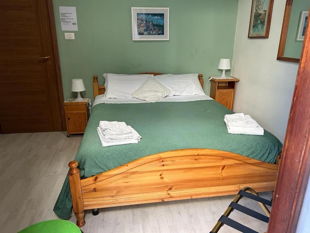 Ein ordentlich bezogenes Bett mit einer grünen Tagesdecke, zwei weißen Kissen und einem Holzkopfstück. Es gibt zwei Nachttische mit Lampen sowie ein gerahmtes Bild an der Wand.