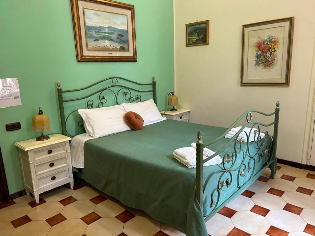 A bed with a green bedspread, white pillows, and a brown pillow, flanked by nightstands with lamps.