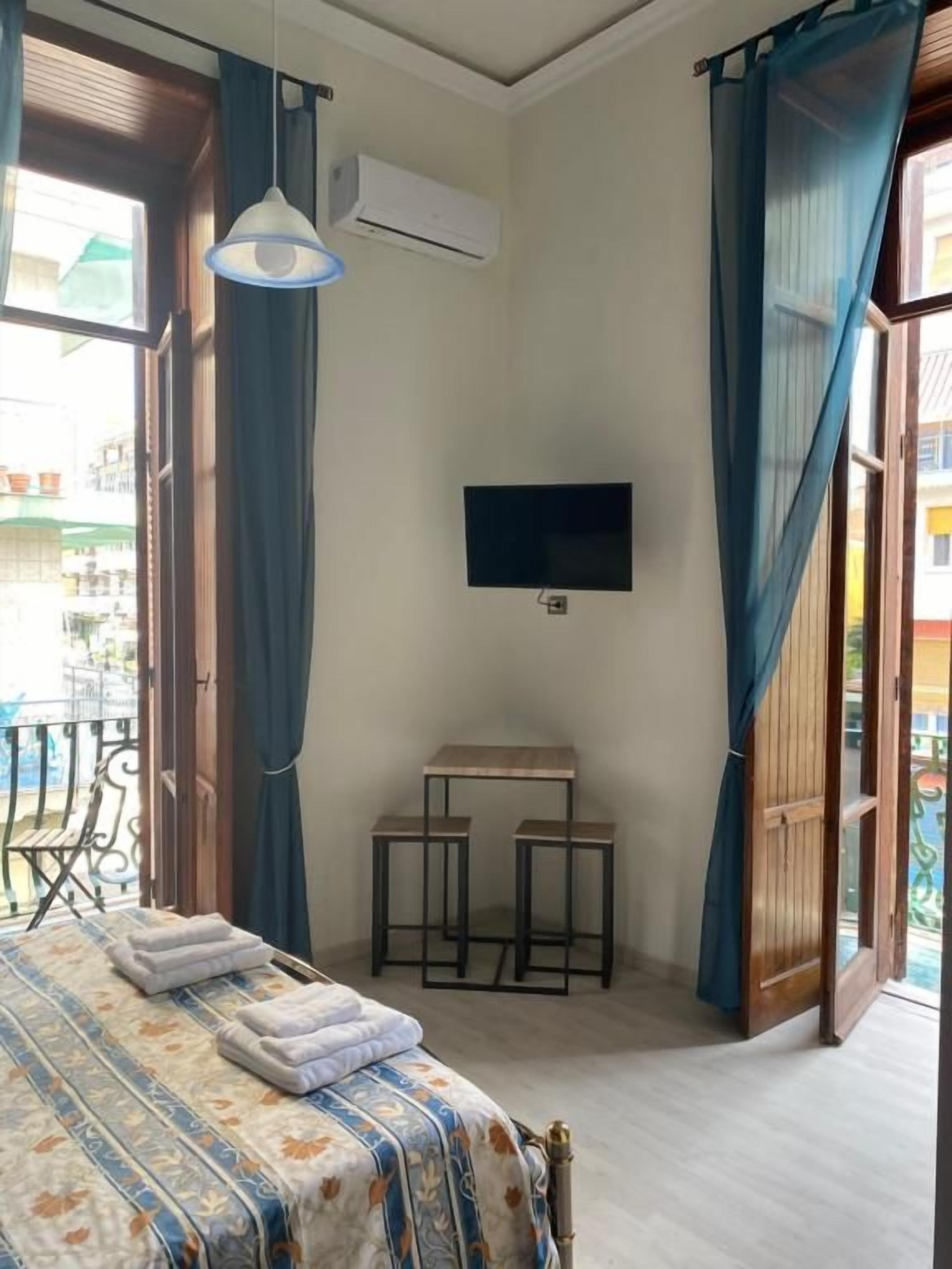 A bedroom with a bed, a TV, a table, and a balcony door.