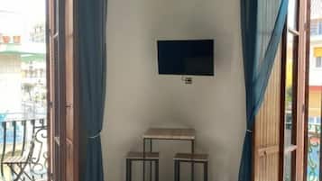 Une chambre avec un lit, une télévision, une table et une porte-fenêtre donnant sur un balcon.