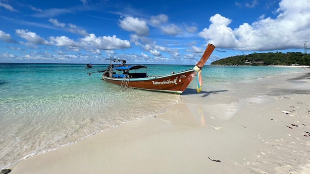 Un bote en una playa despejada con agua turquesa y cielo claro.