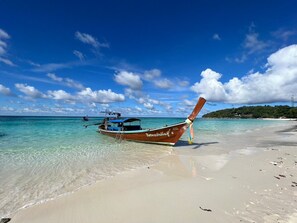 Ein Boot an einem klaren Strand mit türkisblauem Wasser und wolkenlosem Himmel.