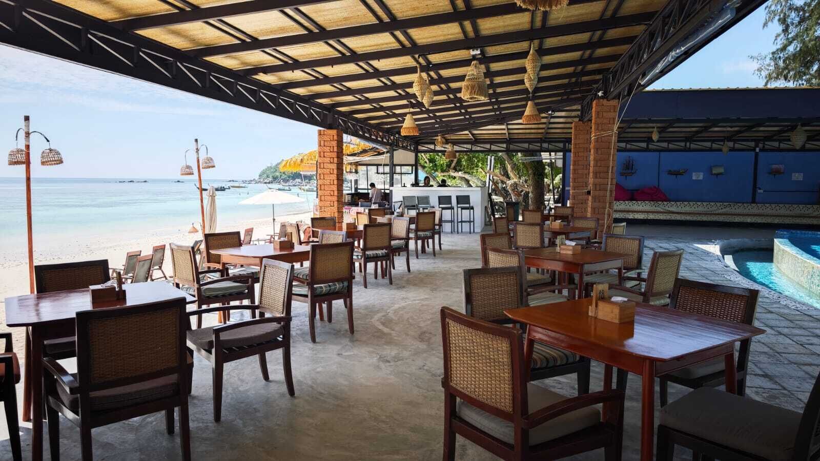 An outdoor dining area with tables and chairs, overlooking a beach and a pool.