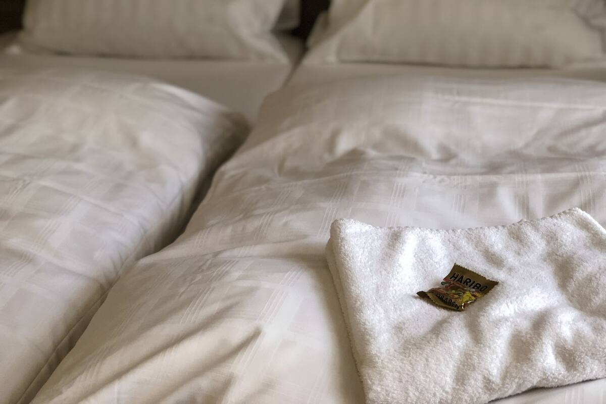 A neatly made bed with white linens and a visible tag on the pillow.