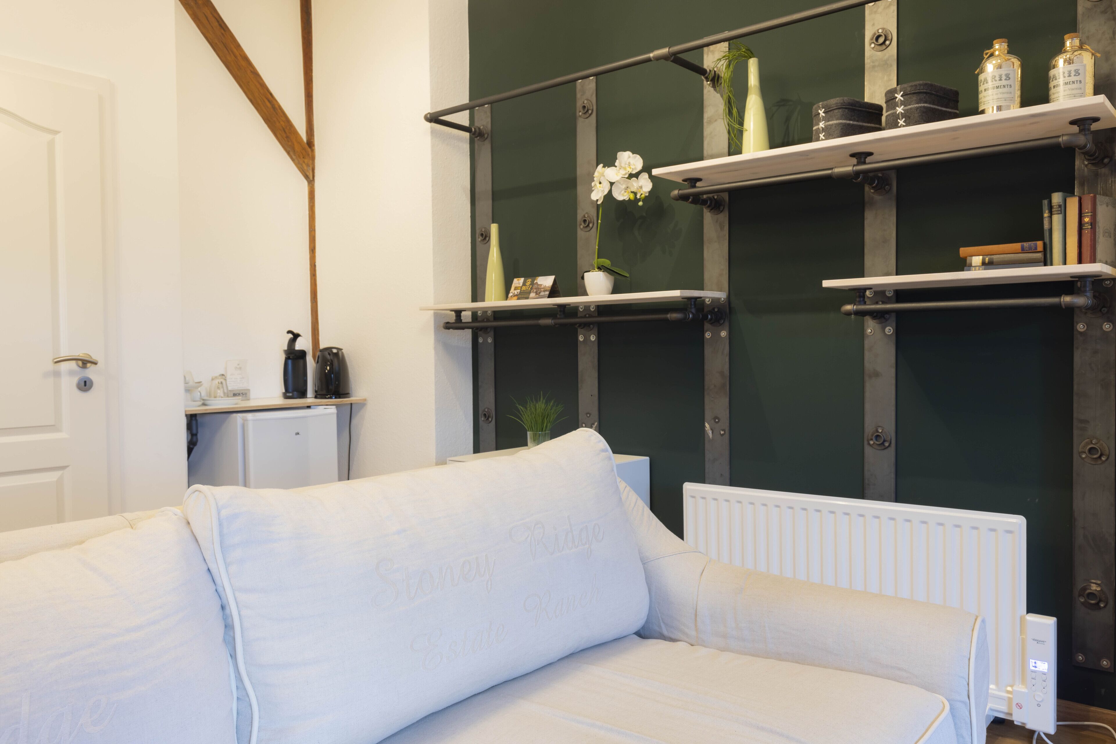A modern living room with a white sofa, a radiator, and shelves with decorative items.