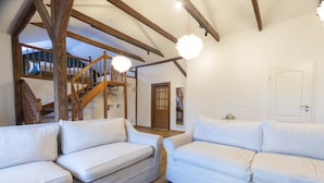 Un salon spacieux avec un escalier en bois, des canapés blancs et une plante en pot.