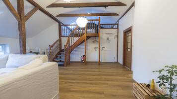 Ein geräumiges Zimmer mit einer Holztreppe zu einer oberen Ebene, einem weißen Sofa und einer hölzernen Bank.