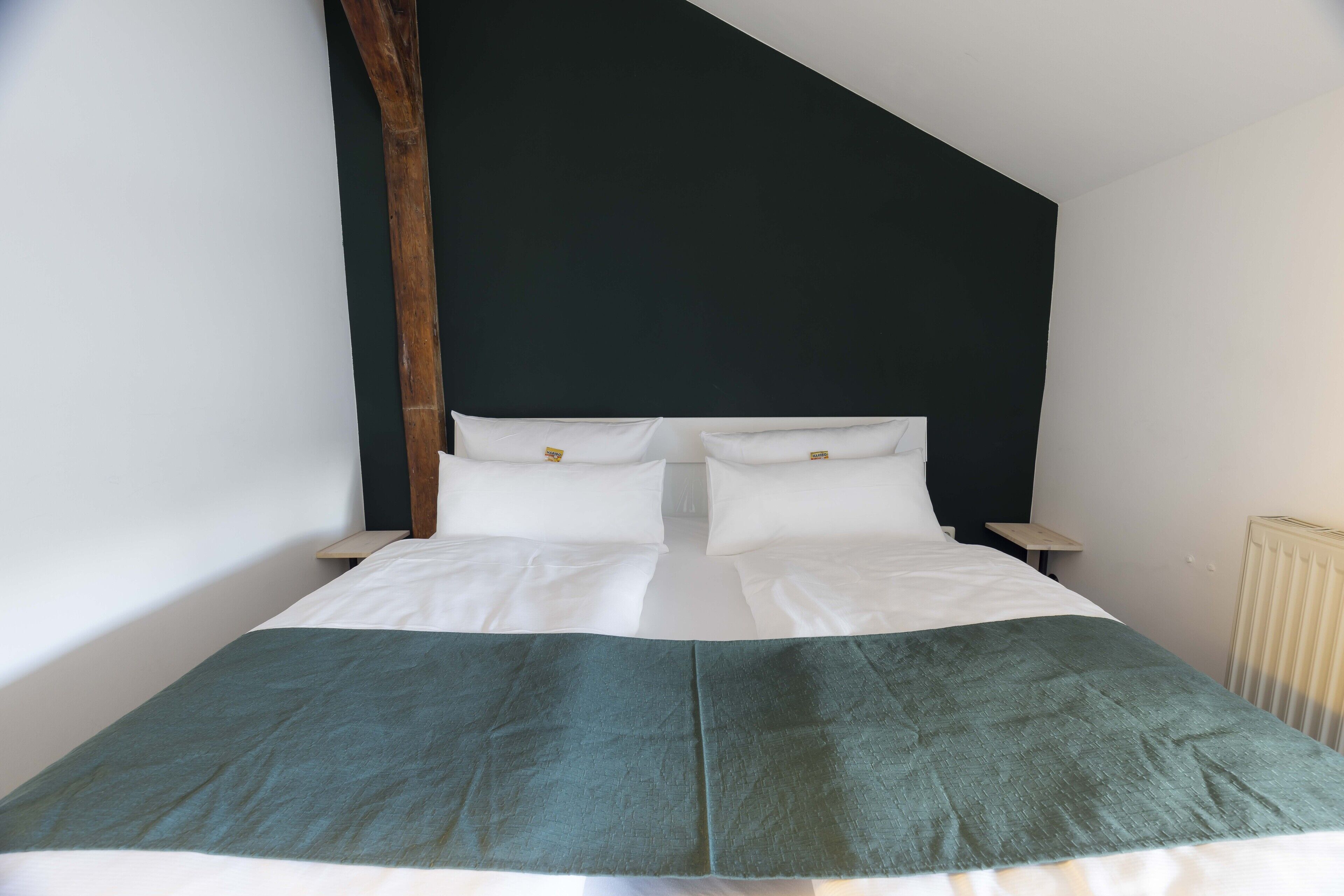 A bed with white linens and a green blanket, a wooden headboard, and a white radiator.