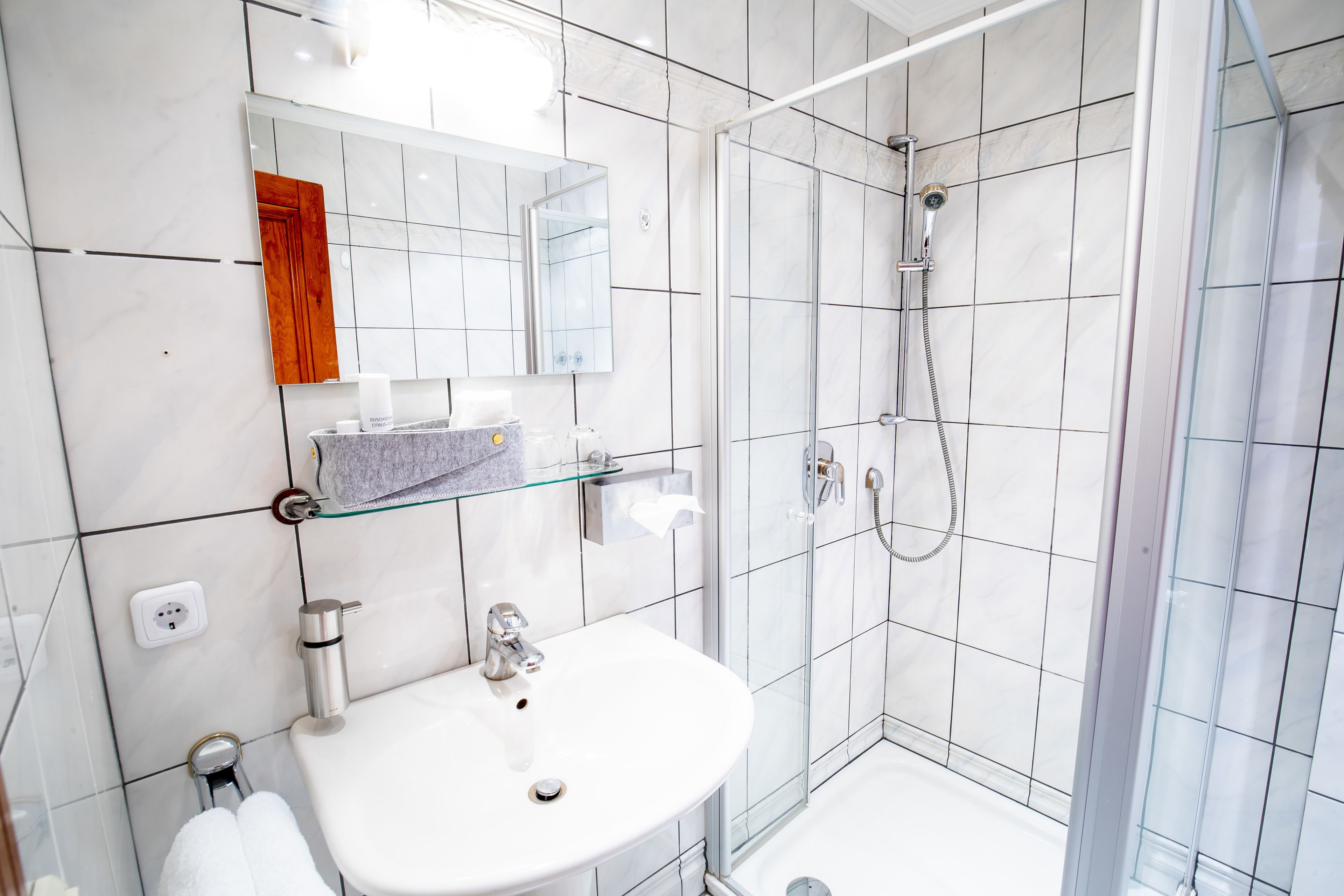 Un bagno moderno con cabina doccia in vetro, un lavandino bianco e uno specchio con cornice in legno.