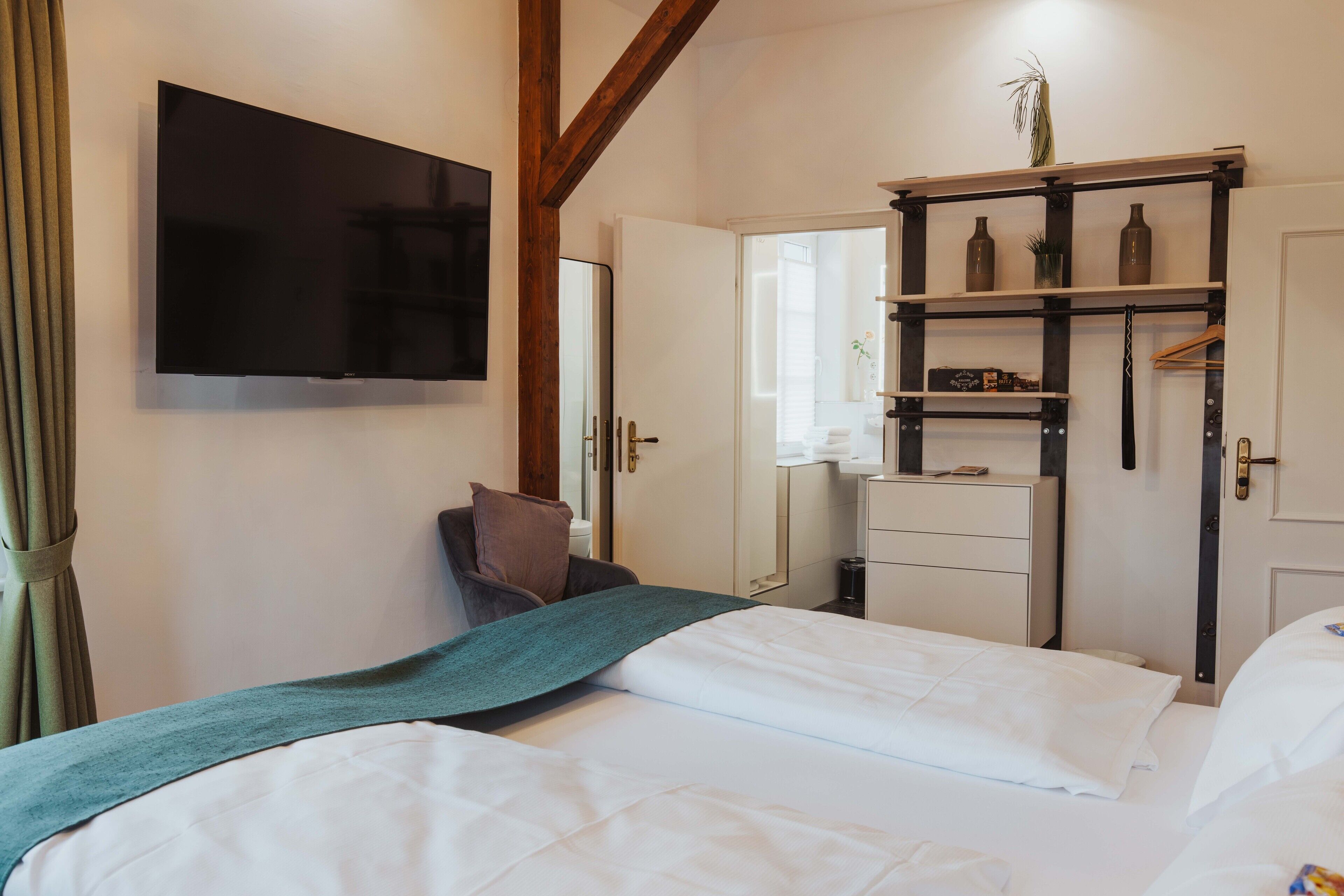 A hotel room with a bed, a television mounted on the wall, a wardrobe, and a mirror.