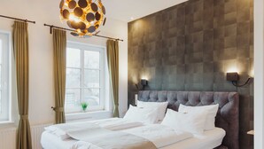 Un lit double bien fait, avec une tête de lit capitonnée, une fenêtre avec des rideaux et un luminaire fixé au mur.