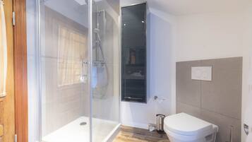 Un baño moderno con ducha envuelta en vidrio, inodoro blanco y suelo de madera.