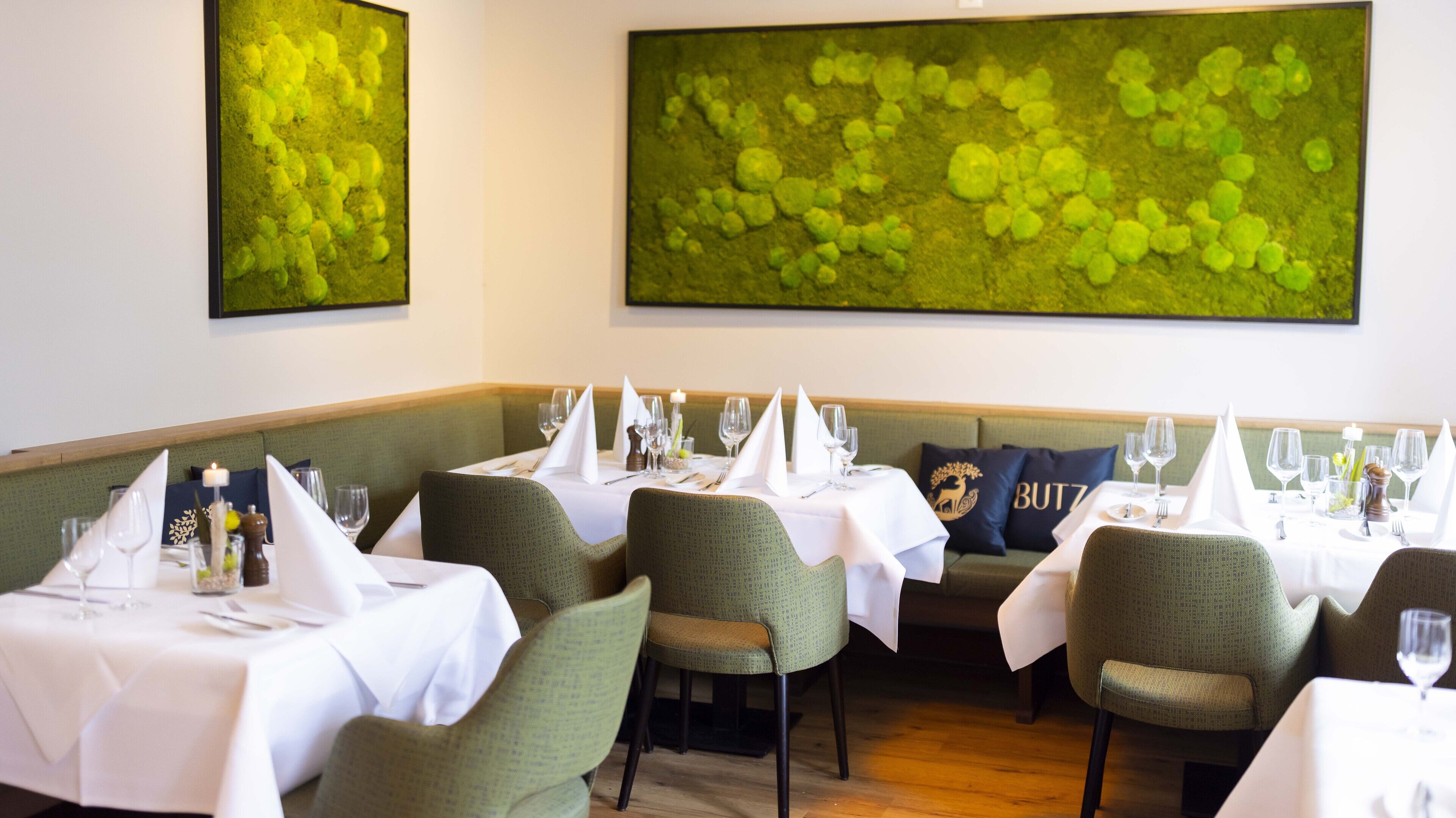 A restaurant with tables set for dining, green upholstered chairs, and a large green abstract painting on the wall.