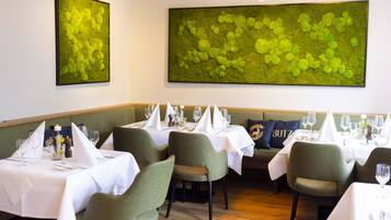 A restaurant with tables set for dining, green upholstered chairs, and a large green abstract painting on the wall.