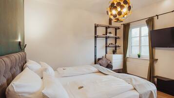 Un dormitorio con cama, mesita de noche, televisor, ventana con cortinas y lámpara colgante.