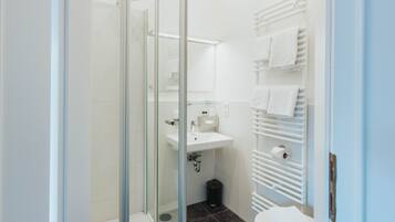 Un baño moderno con cabina de ducha de vidrio, lavabo blanco y toallero.