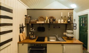 A compact kitchen with wooden countertops, a built-in oven, a sink, and a wall-mounted shelf with kitchen utensils and decorative items. - Sea Side Cottages (Eyrarbakki)