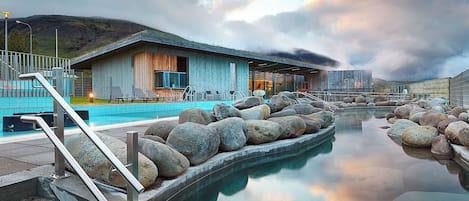 Um edifício moderno com área de piscina, apresentando uma piscina revestida em pedra, assentos externos e vista para a paisagem circundante.