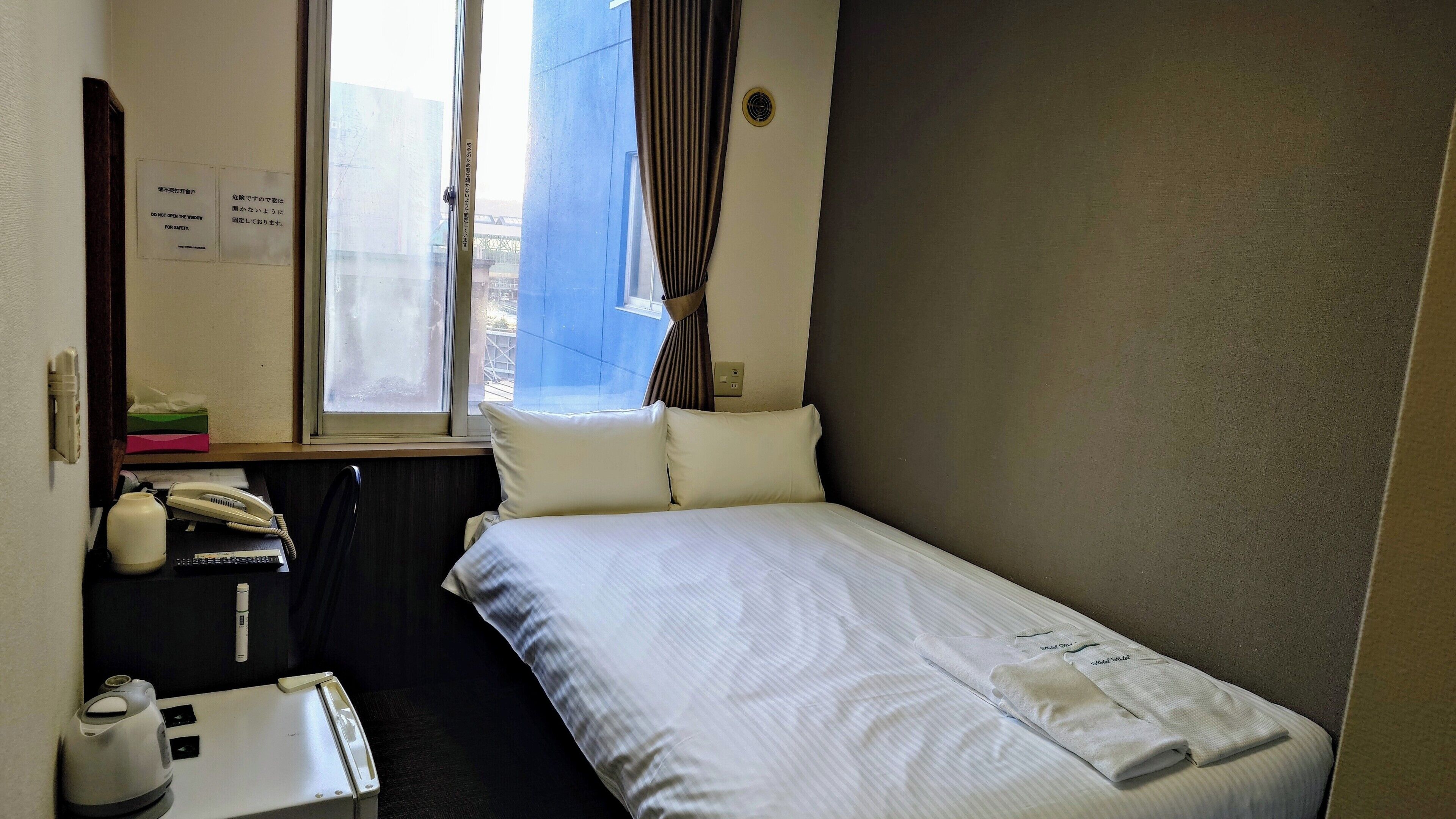 Ett hotellrum med en säng, ett skrivbord med en telefon, en vattenkokare och ett litet bord med en fjärrkontroll.