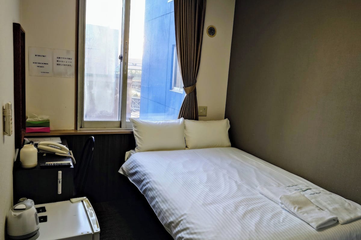 Habitación de hotel con cama, escritorio, teléfono, hervidor de agua y una mesita con control remoto.