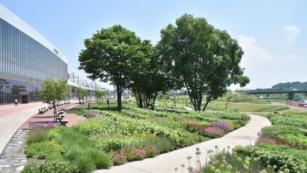 A landscaped garden with a pathway, trees, and a modern building.