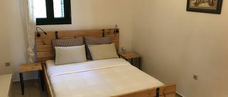 A bedroom with a wooden bed, two bedside tables, a window with curtains, and a framed picture on the wall.