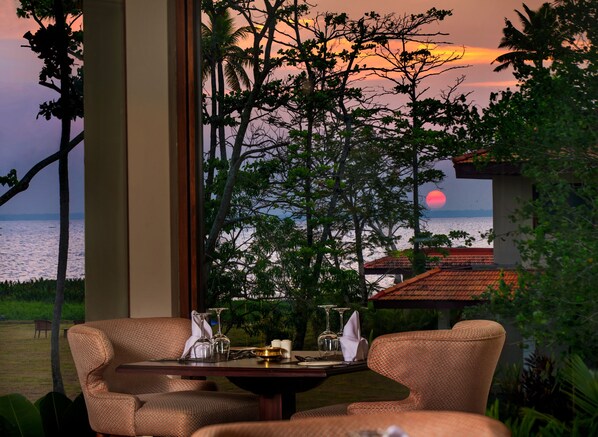 A dining area with a table set for two, overlooking a sunset view of the sea and palm trees. - Niraamaya Retreats Backwaters & Beyond (Kottayam)