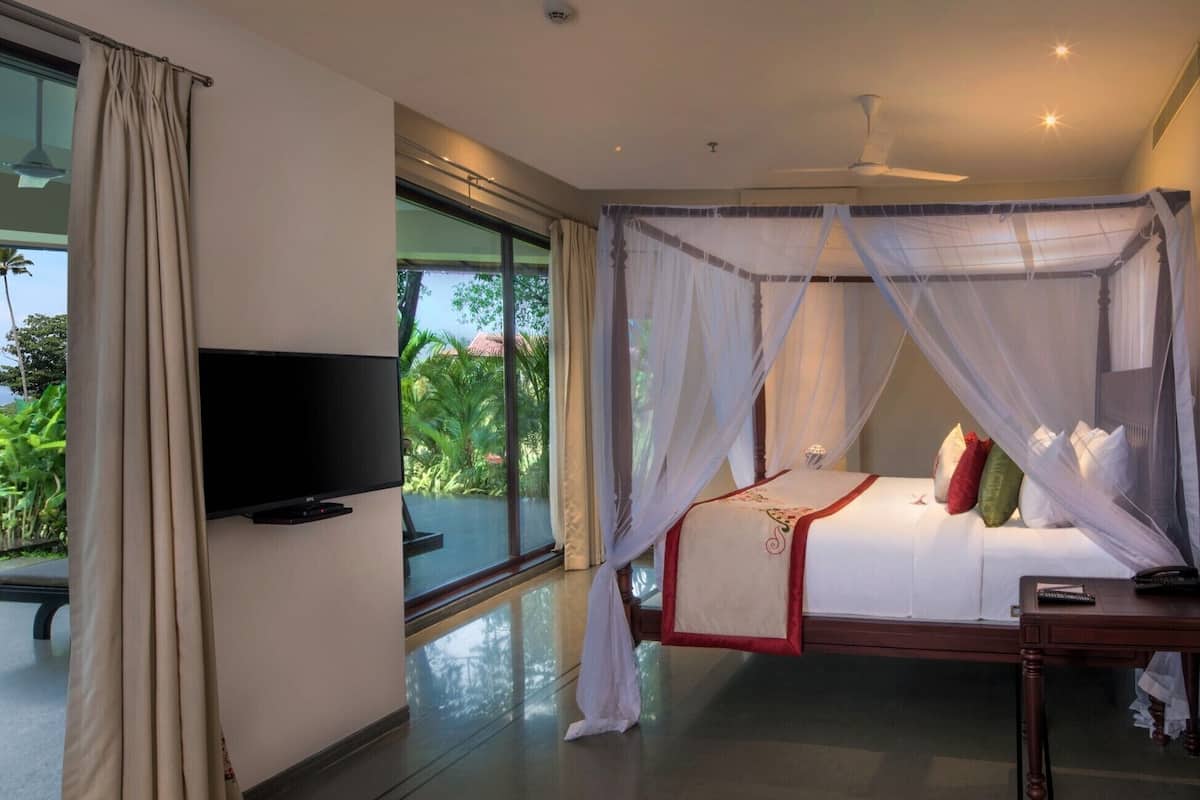 Ein Schlafzimmer mit Baldachinbett, Fernseher und Blick auf Grünfläche.