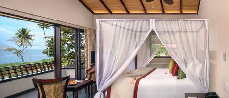 A bedroom with a bed, a chair, a table, and a view of the ocean.