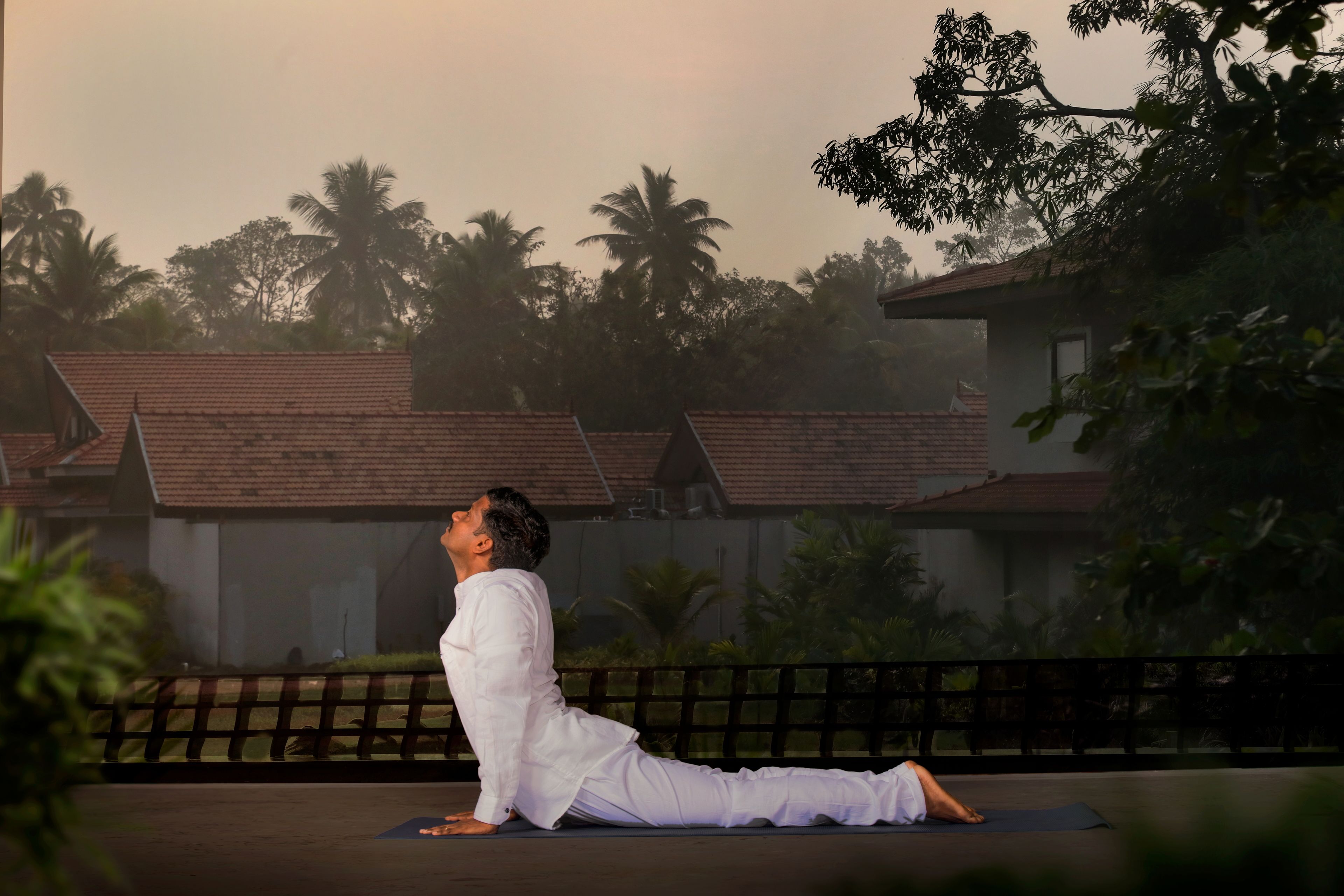 A person performing a yoga pose on a mat outdoors with a view of houses and palm trees in the background.