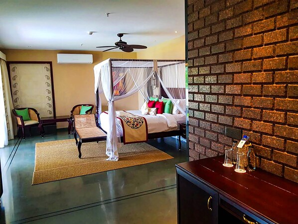 A hotel room with a four-poster bed, a ceiling fan, a brick wall, and a minibar. - Niraamaya Retreats Backwaters & Beyond (Kottayam)
