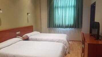 Habitació d'hotel amb dos llits, un escriptori, una cadira, una televisió i una finestra amb cortines.