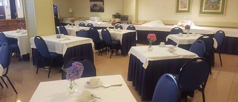 Un comedor con varias mesas dispuestas para el servicio, sillas y un cuadro colgado en la pared.