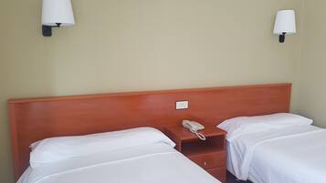 Una habitación de hotel con dos camas individuales, cabecera de madera, mesitas de noche y lámparas de pared.