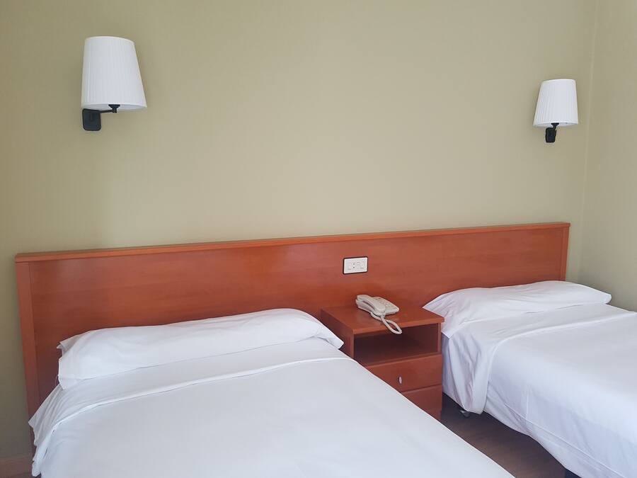 Una habitación de hotel con dos camas individuales, cabecera de madera, mesitas de noche y lámparas de pared.
