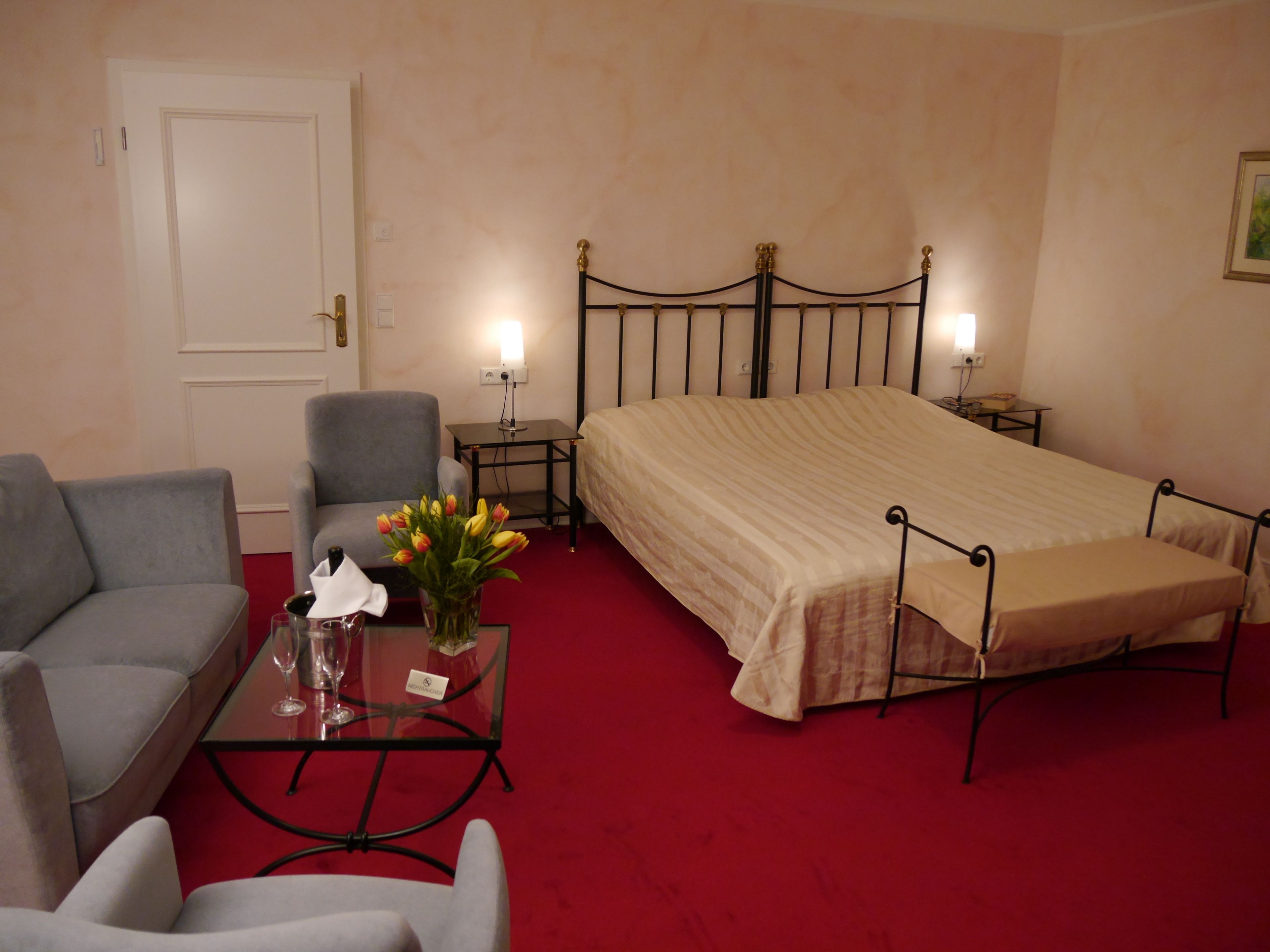 Une chambre d’hôtel avec un lit, un canapé, une petite table ornée d’un vase de fleurs et une table de chevet avec une lampe.