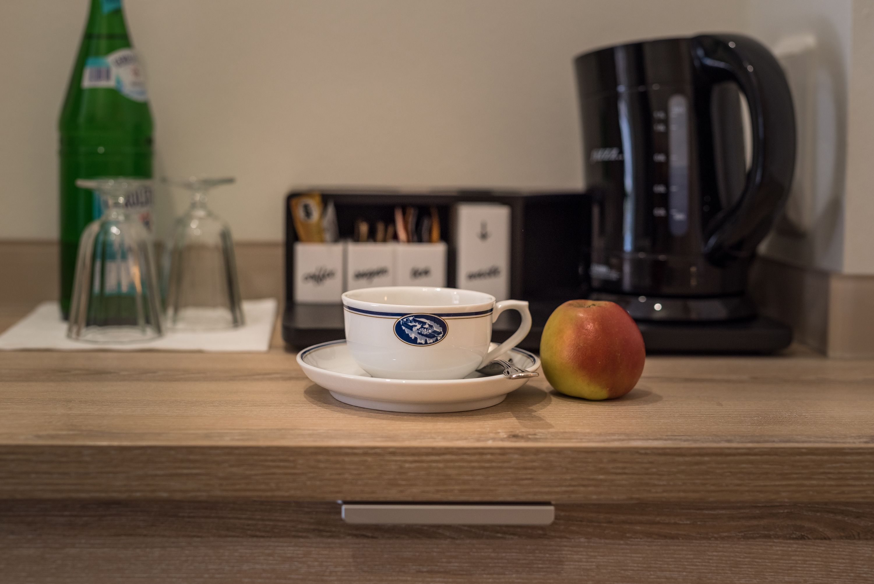 Una encimera de cocina con una cafetera, una taza con un logotipo, un vaso y una botella.