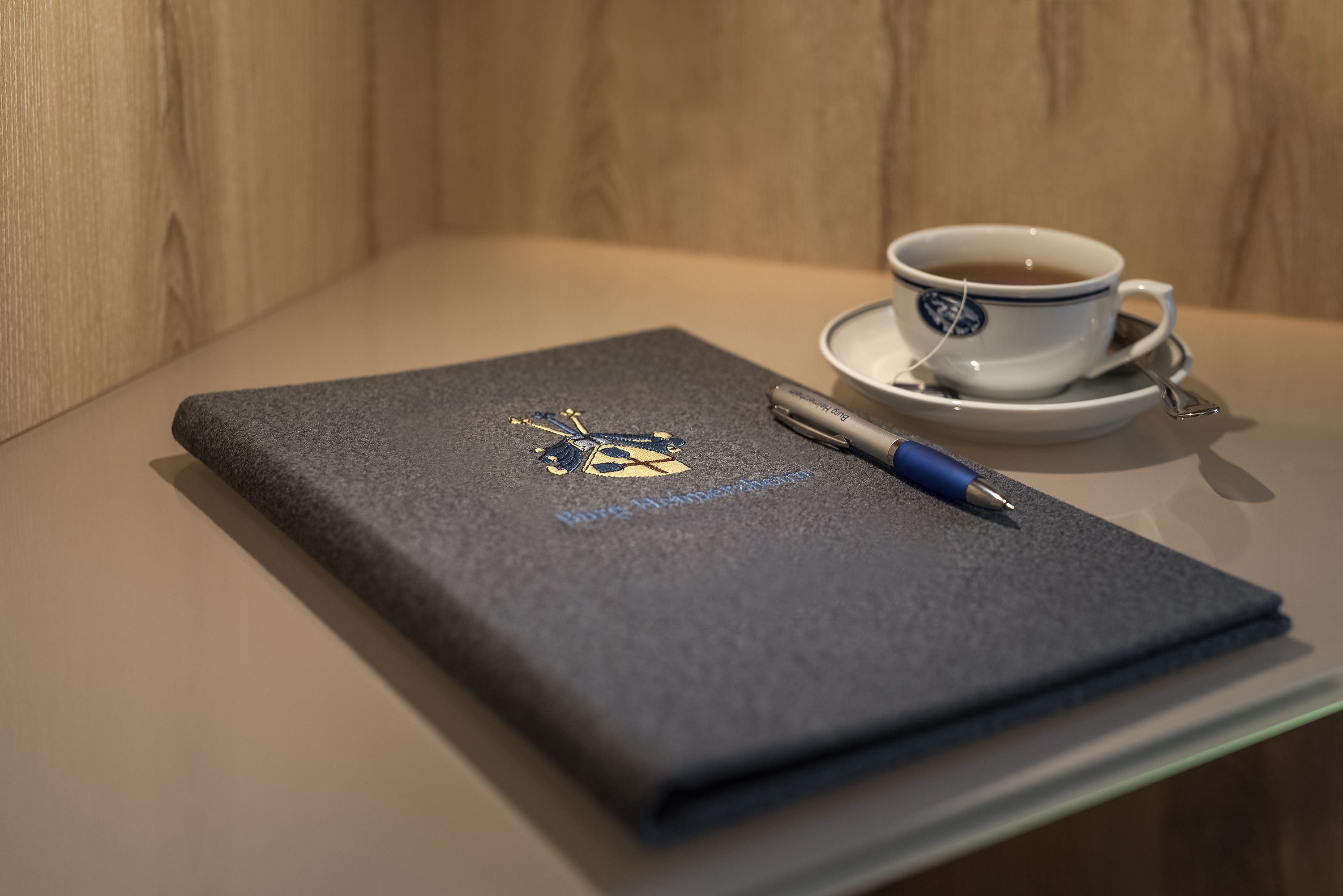 Um caderno com uma caneta e uma chávena de chá sobre uma mesa.