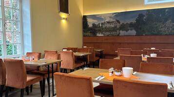 Un espace repas comprenant plusieurs tables et chaises, un grand tableau accroché au mur et une fenêtre donnant sur un paysage verdoyant.