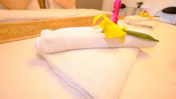 A neatly folded white towel with a yellow flower on a hotel bed.