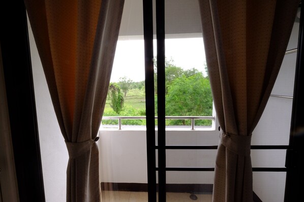 A view through a window with curtains tied back, revealing a balcony with a railing and greenery outside. - Tafah Residence (Sakon Nakhon)