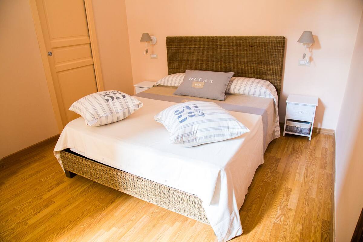 Una cama doble con cabecera trenzada, dos mesitas de noche y una mesilla.