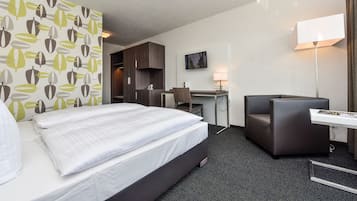 Una habitación de hotel con cama, escritorio, silla y televisor en la pared.