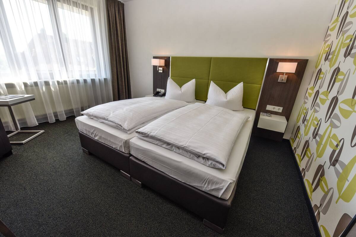 A hotel room with two beds, a desk, and a view of the city through large windows.
