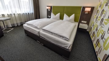 A hotel room with two beds, a desk, and a view of the city through large windows.
