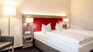 A hotel room with a large bed, a wooden headboard, two bedside lamps, a small nightstand, and a chair.